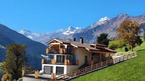 Een huis met twee verdiepingen en een balkon, gelegen tegen een bergachtige achtergrond.