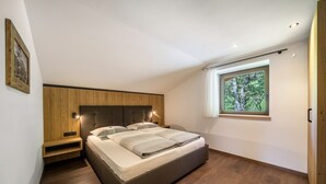 Een moderne slaapkamer met een groot bed, een vastgezet houten hoofdbord, nachtkastjes en een raam met uitzicht op bomen.
