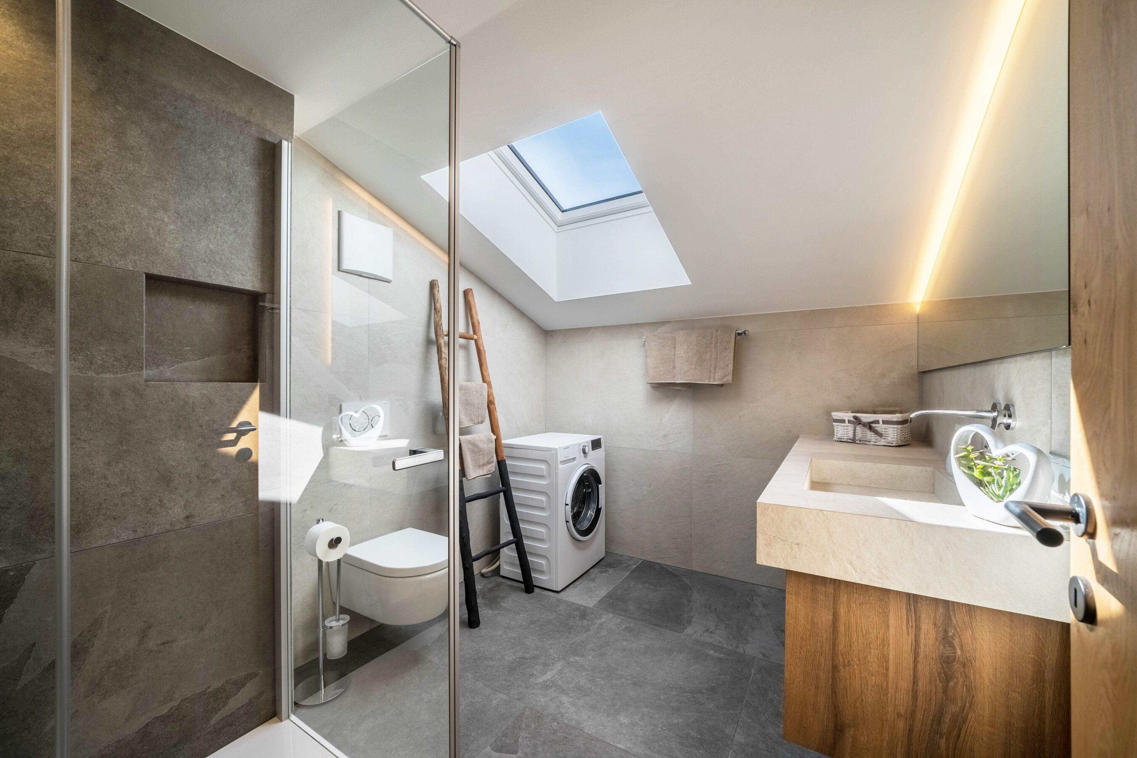 Un baño moderno con tragaluz, lavadora y tocador de madera.