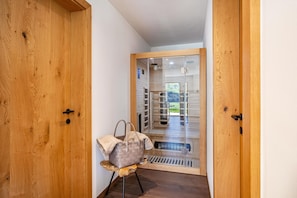 Une porte en bois avec un panneau de verre, un banc en bois sur lequel se trouve un sac, et une vue sur un balcon.