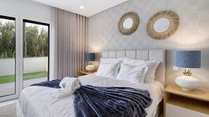 Ett modernt hotellrum med en stor säng, två sängbord, en stor spegel och utsikt över grönområden genom den skjutbara glasdörren.
