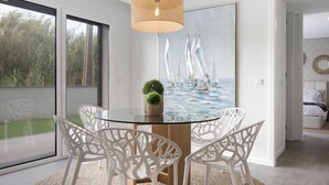 En matplats med ett glasbord, vita stolar, en stor krukväxt i mitten och en tavla som föreställer segelbåtar.