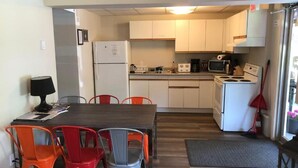 Uma cozinha compacta com armários brancos, geladeira, micro-ondas, fogão e um espaço de refeições com mesa e cadeiras.