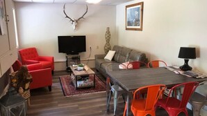 Uma sala de estar com sofá, cadeiras vermelhas, mesa de jantar, televisão e decoração de crânio de veado.