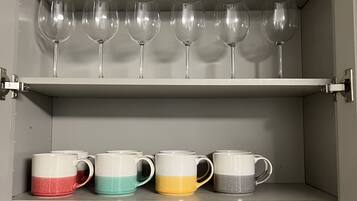 A storage cabinet with shelves holding wine glasses, ceramic mugs, and clear drinking glasses.