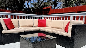Un sofá modular con cojines rojos sobre una terraza blanca con una mesa de centro de vidrio.