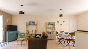 A living room with a sofa, TV, and dining area with chairs and a table. - Holiday Home "Begognias" with Private Terrace (LE CHATEAU-D'OLERON)