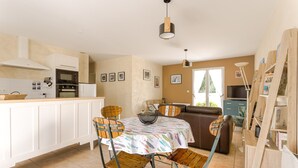 A kitchen with white cabinets, a dining table with chairs, a sofa, and a TV. - Holiday Home "Begognias" with Private Terrace (LE CHATEAU-D'OLERON)