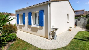 A white building with blue shutters, a small outdoor sink, and a gravel driveway. - Holiday Home "Begognias" with Private Terrace (LE CHATEAU-D'OLERON)