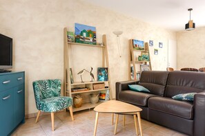 Un salon comprenant un canapé, un fauteuil, une table basse, un téléviseur et des étagères remplies de livres et d’objets décoratifs.