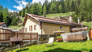 A rustic house with a sloped roof, surrounded by a wooden fence, and set against a mountainous backdrop.