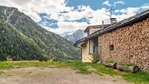 A rustic building with a stone wall and a wooden roof, surrounded by a mountainous landscape.