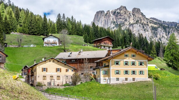 A mountain village with traditional wooden houses, a prominent mountain in the background, and a road leading up the hill.