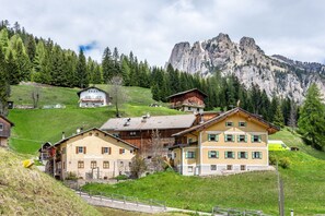 Ein Bergdorf mit traditionellen Holzhäusern, ein markanter Berg im Hintergrund und eine Straße, die den Hügel hinaufführt.
