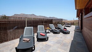 A rooftop terrace with lounge chairs, a table, and a view of mountains.