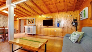A wooden interior with a sofa, a table, a TV, and a fan.