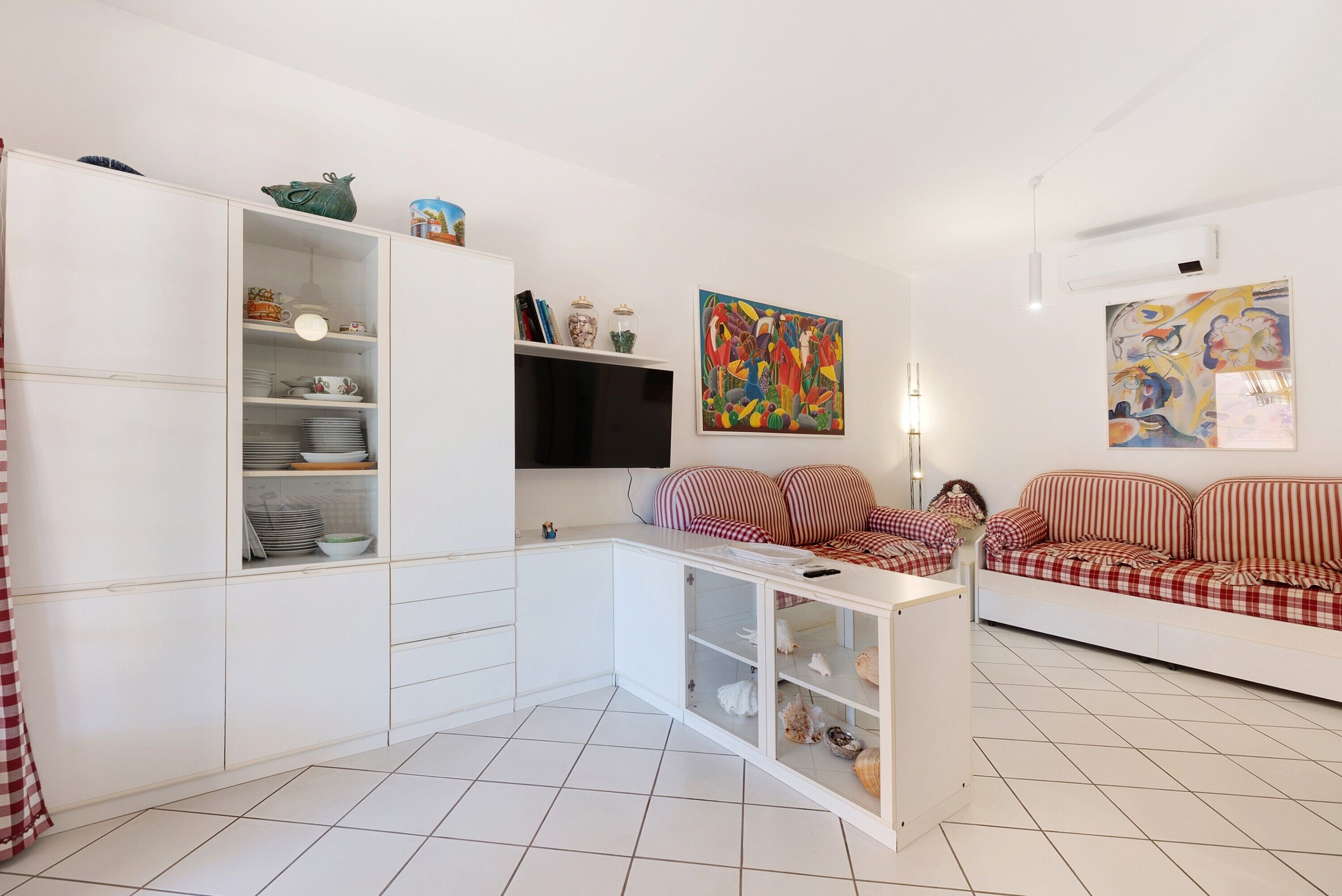 Ein modernes Wohnzimmer mit einer weißen Sofagarnitur, einem Flachbildfernseher und einem Essbereich mit weißen Schränken.