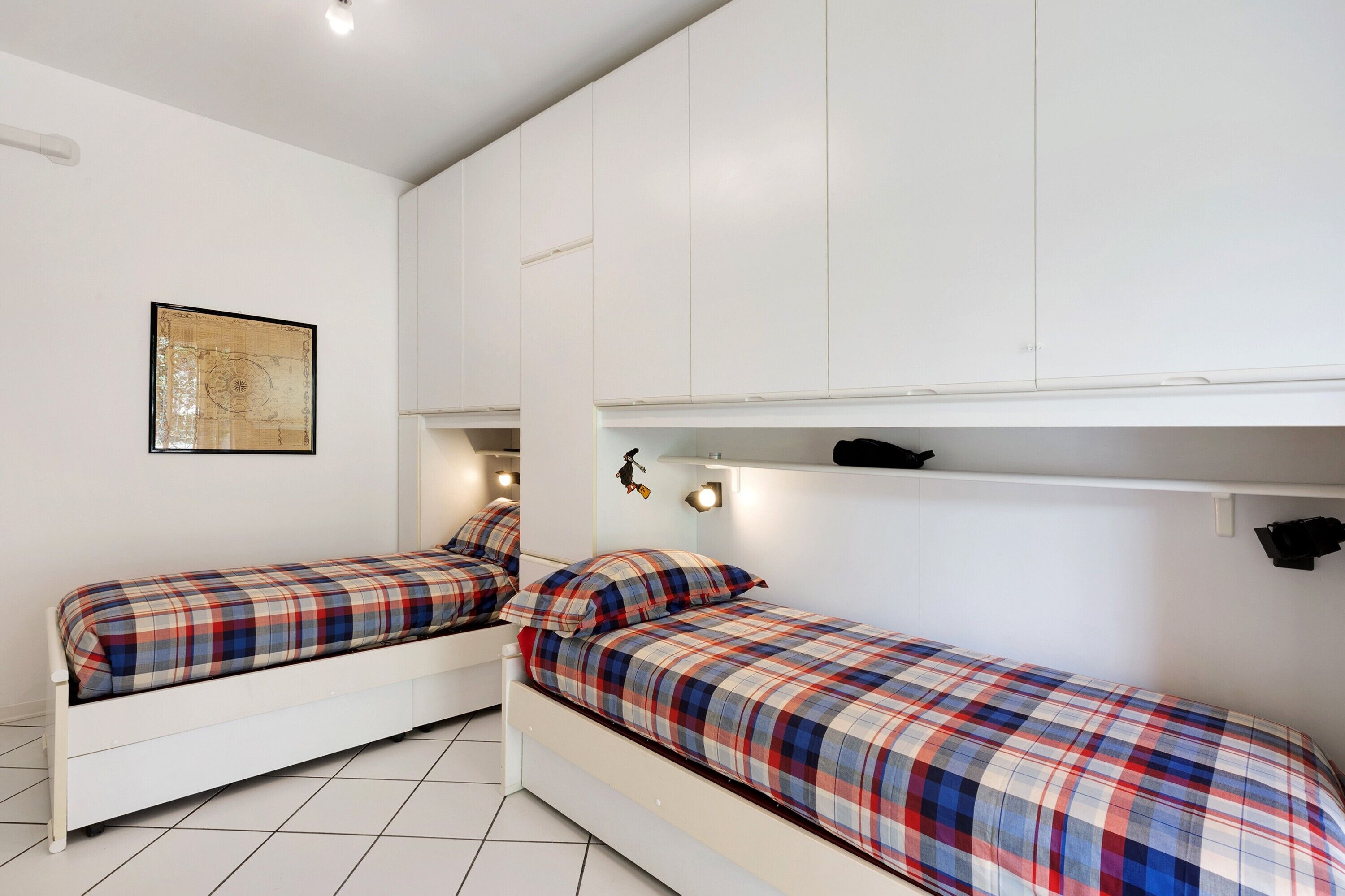 Une chambre avec deux lits simples, des murs blancs, un tableau encadré et des placards intégrés.