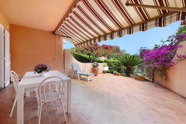 Une terrasse extérieure avec une table et des chaises, un auvent à rayures et des plantes en pot.
