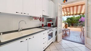 Eine Küche mit weißen Schränken, einer Spüle, einer Mikrowelle und einer Waschmaschine. Es gibt eine Terrasse mit Tisch und Stühlen.