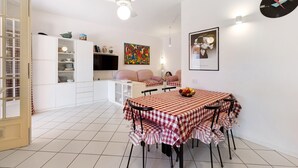 Ein Essbereich mit kariertem Tischlaken, einem Deckenventilator, einer Uhr und einem farbenfrohen Bild an der Wand.