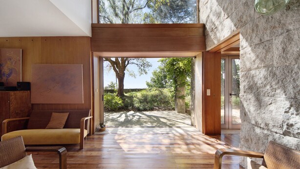 Ein modernes Interieur mit Holzboden, einer Couch und einem großen Fenster mit Blick auf einen Garten.