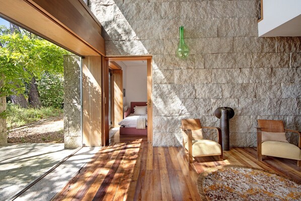 A modern interior with a stone wall, wooden flooring, and a bed in the background.