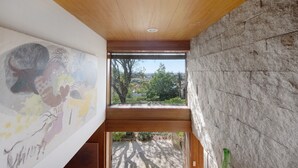 Ein Zimmer mit Holzbalkendecke, Steinwand und Blick ins Grüne.