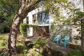 A modern building with large windows, a tree in the foreground, and outdoor seating.