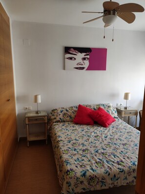 A bedroom with a bed, two bedside tables, a ceiling fan, and a wall-mounted artwork.