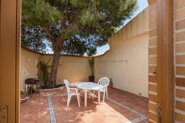 Une terrasse avec une table ronde et des chaises, un pot de fleurs et un barbecue.