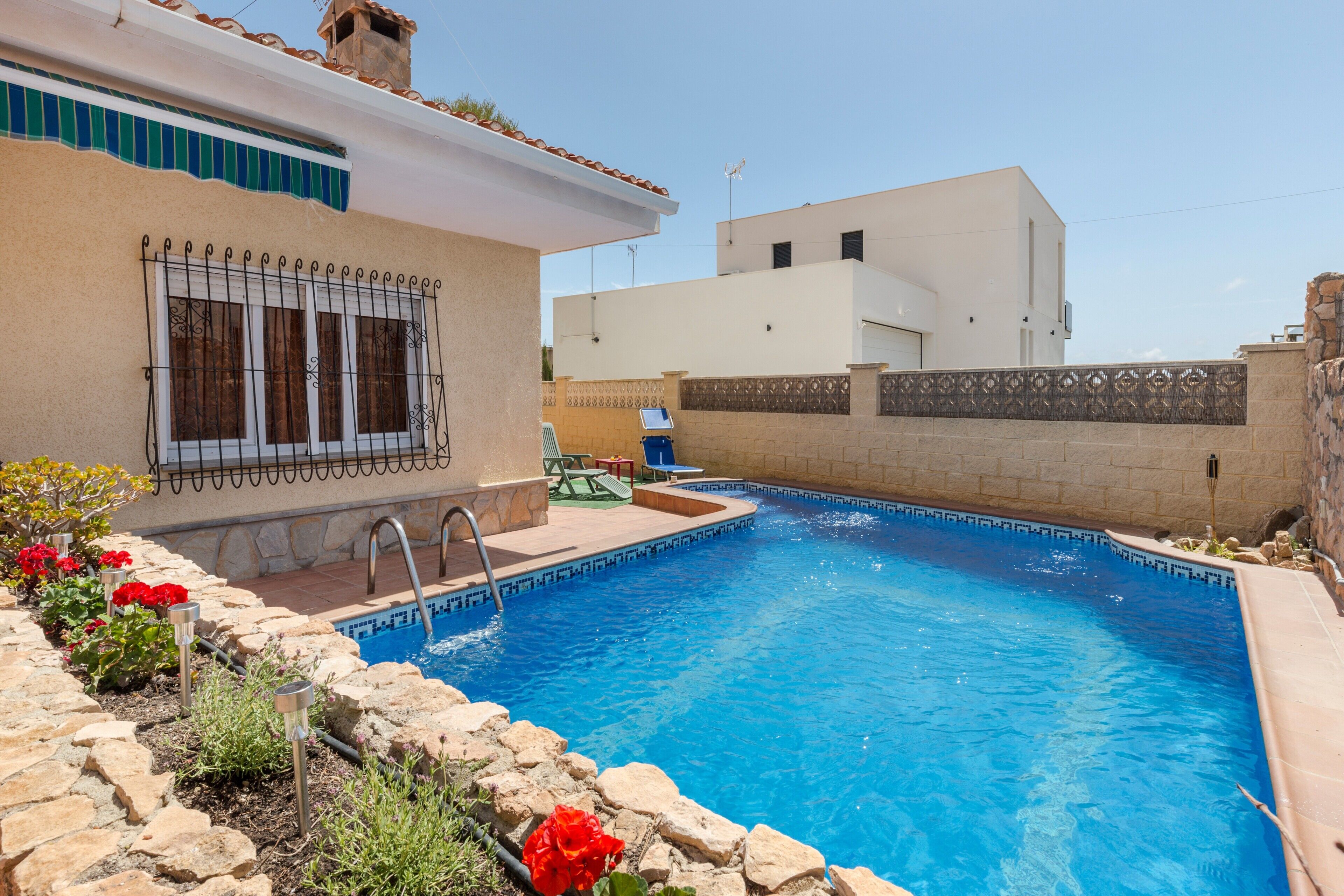 Una piscina con borde de piedra, escalera metálica y una silla.