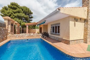 Une piscine avec un mur en pierre et une terrasse carrelée, un patio couvert et un bâtiment en pierre doté d’une fenêtre.