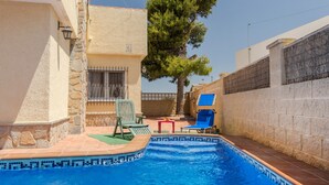 A swimming pool with tiled edges, surrounded by stone walls, and equipped with outdoor furniture.