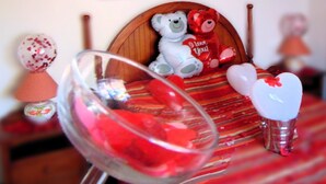 A bed with a teddy bear, a glass of red liquid, and heart-shaped decorations.