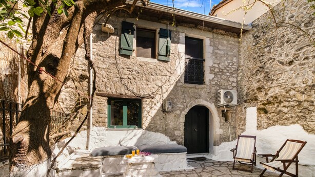 Un edificio de piedra con patio, mobiliario exterior y unidad de aire acondicionado.