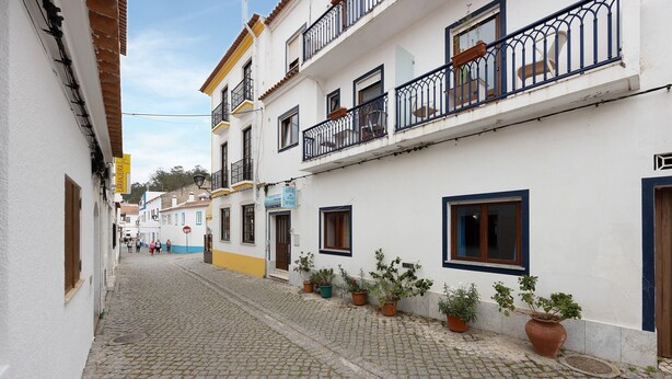 Uma rua de paralelepípedos com edifícios brancos, vasos de plantas e uma placa azul.