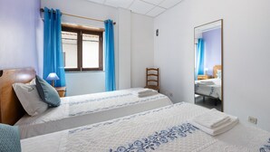 Quarto de hotel com duas camas, cabeceira de madeira, espelho e janela com cortinas azuis.