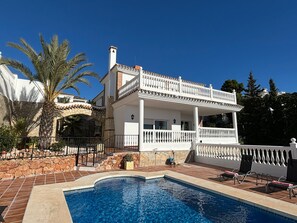 Een tweelaags huis met een zwembad, stenen muren en een wit balkon.