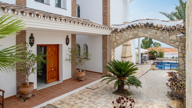 Un edificio blanco con un arco de piedra, una piscina y plantas en macetas.