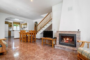 A living room with a fireplace, a dining area with wooden furniture, a TV, and a staircase leading to an upper level.