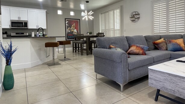Una sala de estar moderna con un sofá gris, un comedor y una cocina con armarios blancos y un microondas.