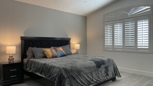 Un dormitorio con cama, mesitas de noche y una ventana con persianas.