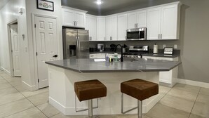 Una cocina moderna con gabinetes blancos, electrodomésticos de acero inoxidable y una isla central con dos taburetes.