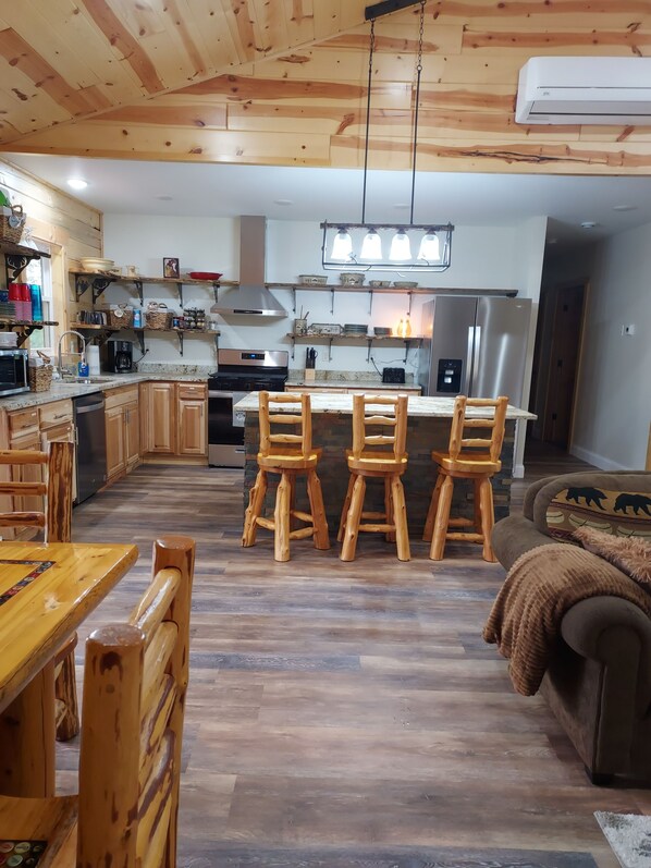 A modern kitchen with wooden cabinets, a central island, and a dining area with wooden chairs. - Finlayson log cabin on 10 acres (Finlayson)