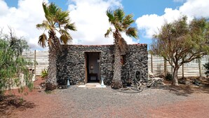 Un bâtiment en pierre avec une porte, des palmiers et un chemin de gravier.