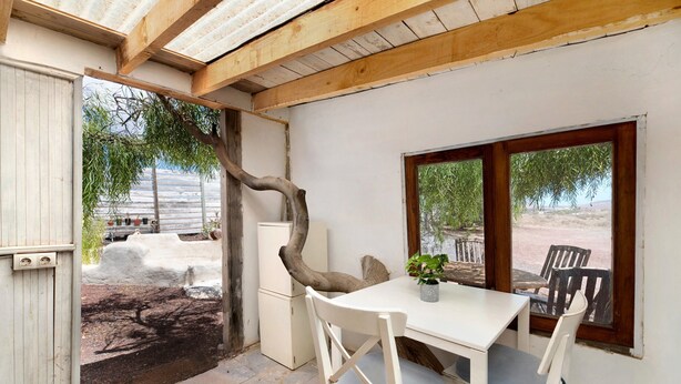 Une pièce avec une table et des chaises blanches, une petite plante en pot, un plafond avec une poutre en bois et une vue sur l’extérieur.