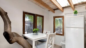 Une pièce avec une table blanche, une chaise, un réfrigérateur et une fenêtre donnant sur des arbres.
