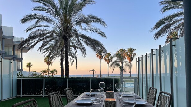 A dining table set for six with chairs, a candle, and a view of the ocean and palm trees. - Apartment 'Residencial Mar De Denia 2' with Sea View, Wi-Fi and Air Conditioning (Denia)