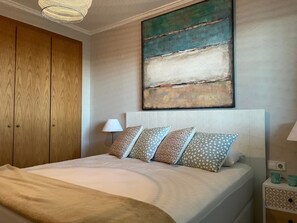 Une chambre à coucher comprenant un lit, une armoire en bois, une table de chevet, une lampe et un grand tableau abstrait accroché au mur.